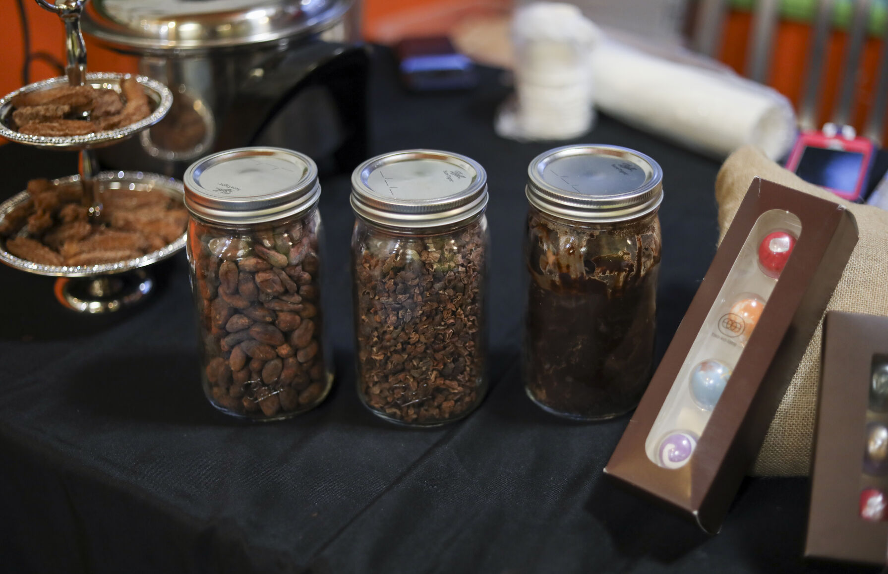 Jars of cacao beans, cacao nibs and chocolate sit in a line